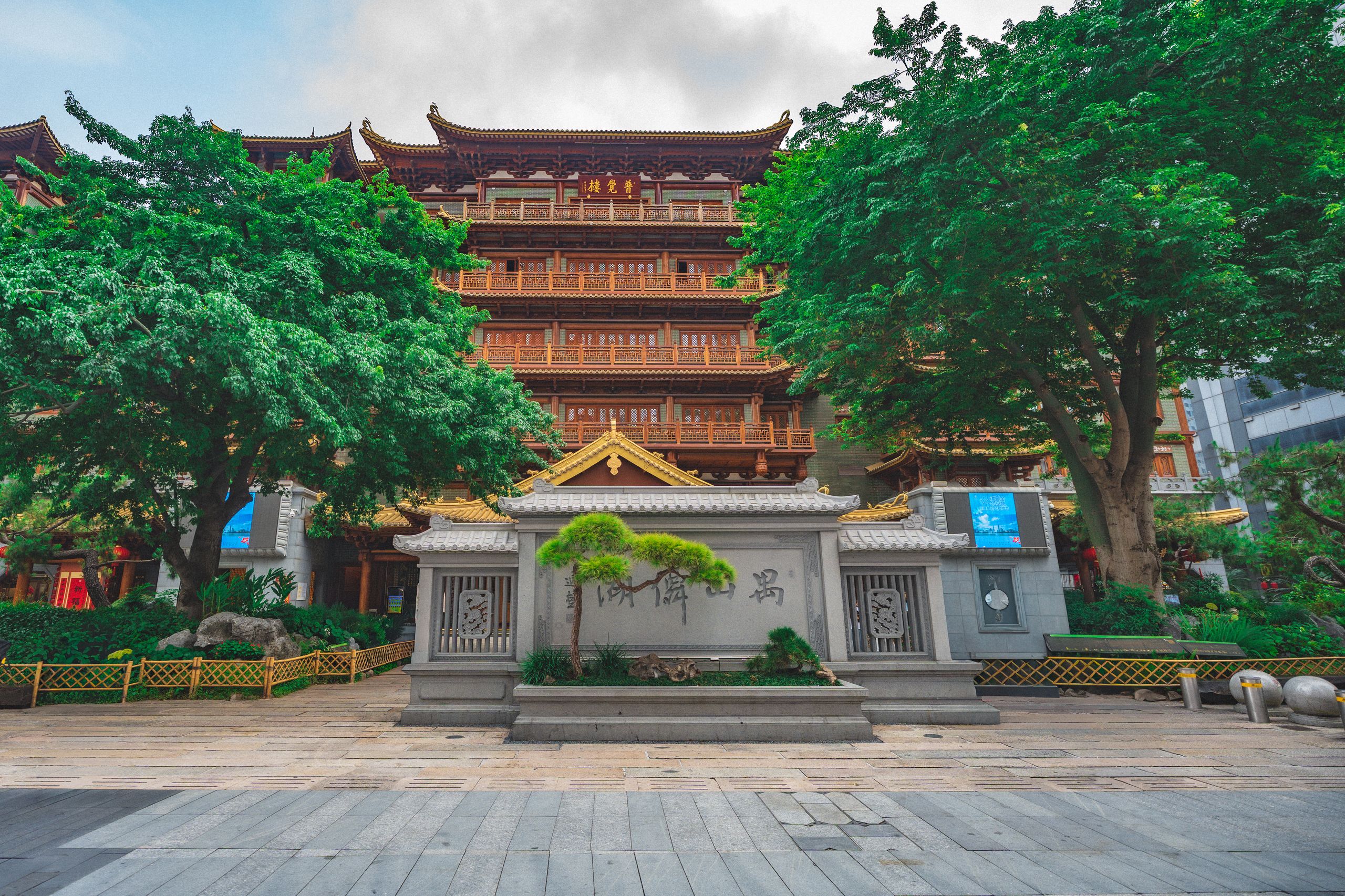 Traditionelles Gebäude im chinesischen Stil hinter einem Steinschild und großen grünen Bäumen