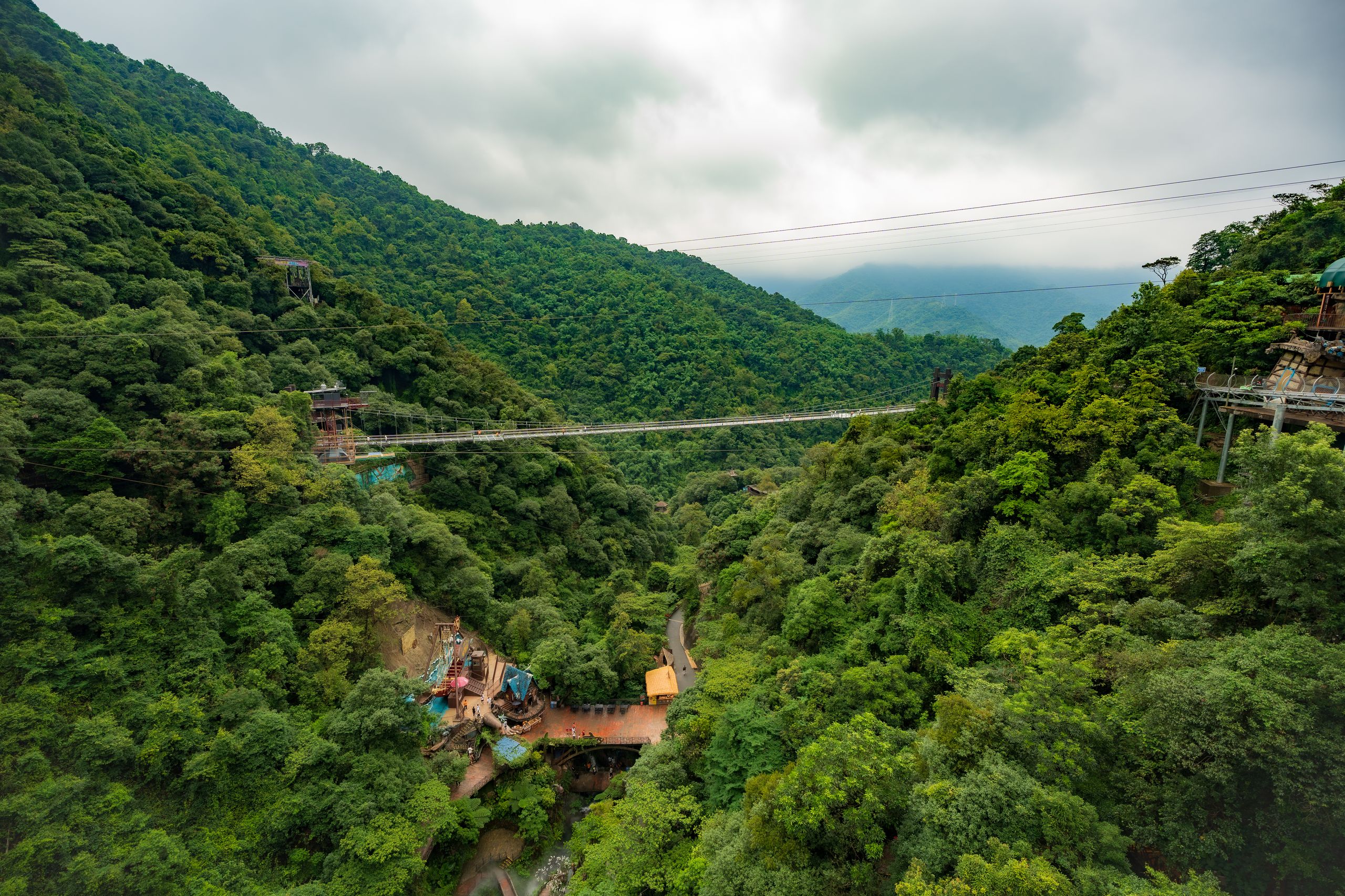 Hängebrücke über einem bewaldeten Bergtal unter bewölktem Himmel
