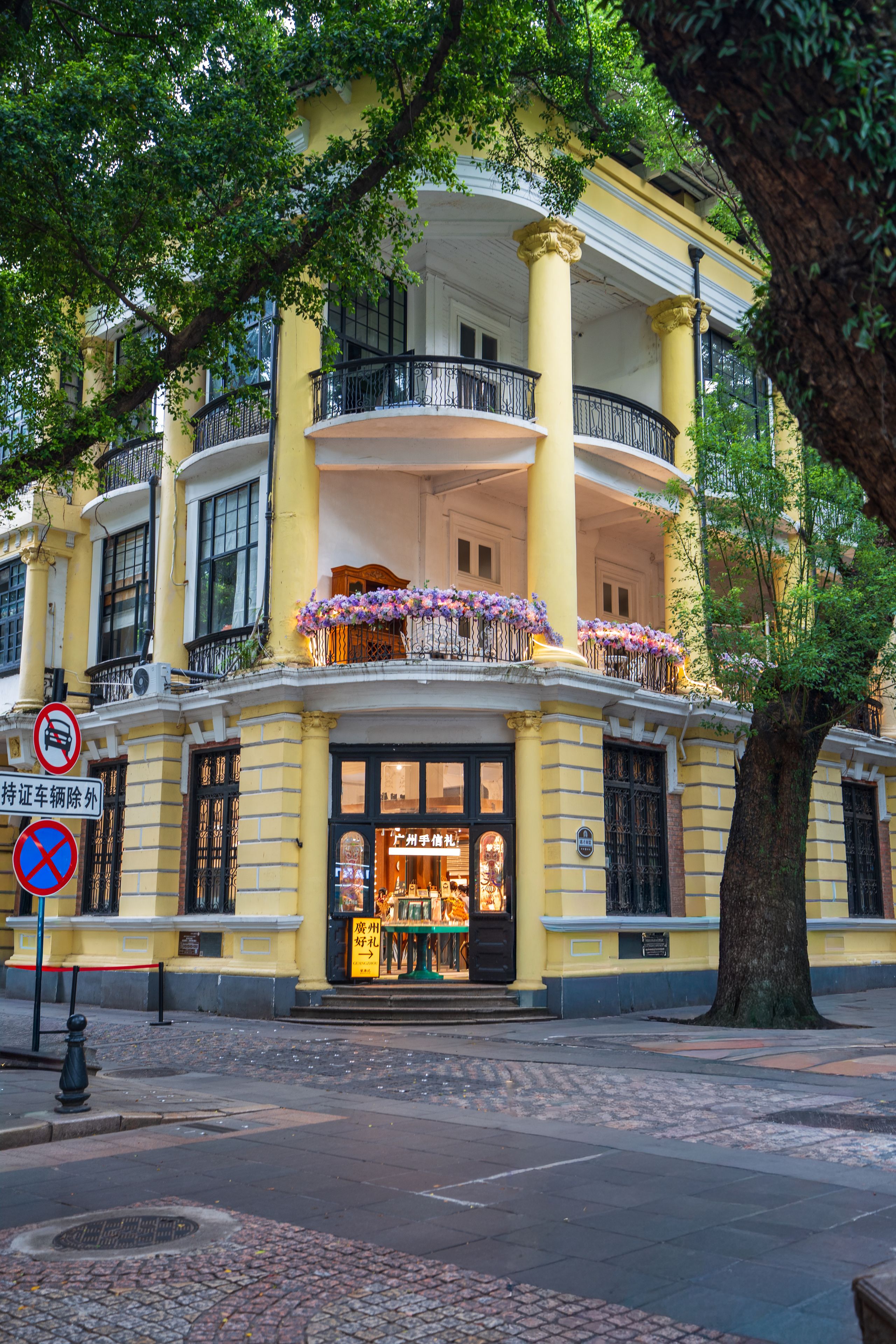 Gelbes Gebäude im Kolonialstil mit Balkonen, Säulen und Bäumen an der Straße