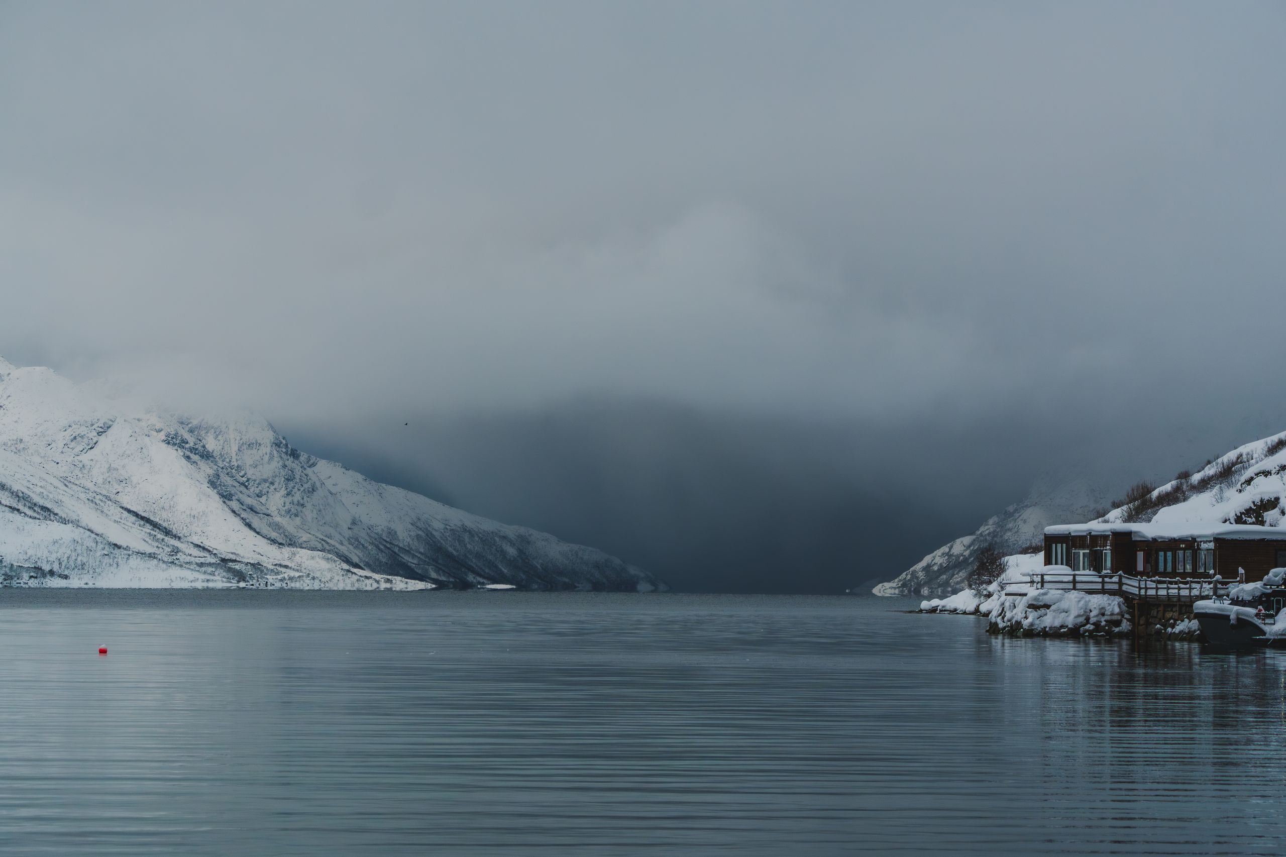 Nebliger Fjord umgeben von verschneiten Bergen