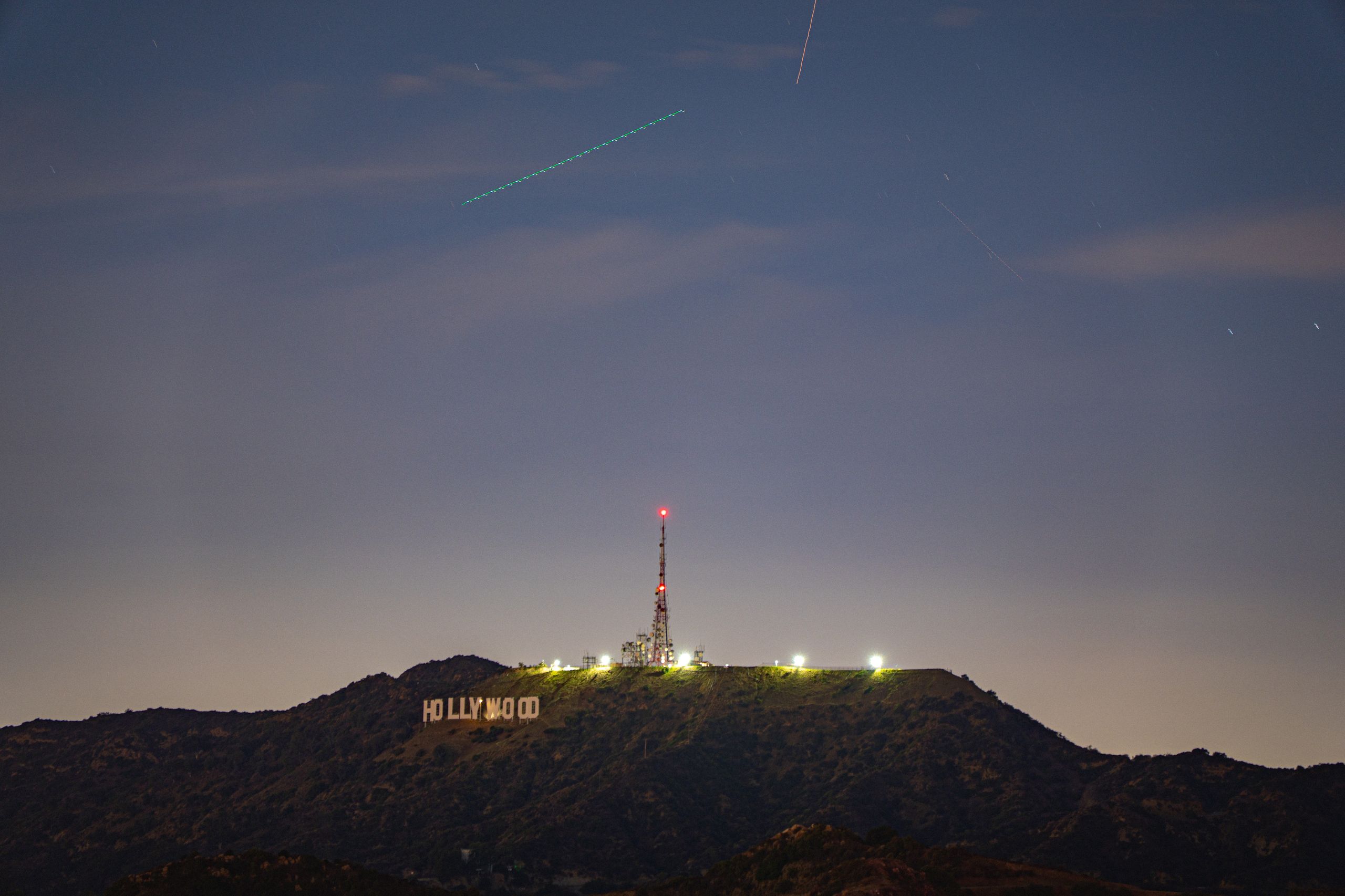 Hollywood sign at night with a plane trail overhead