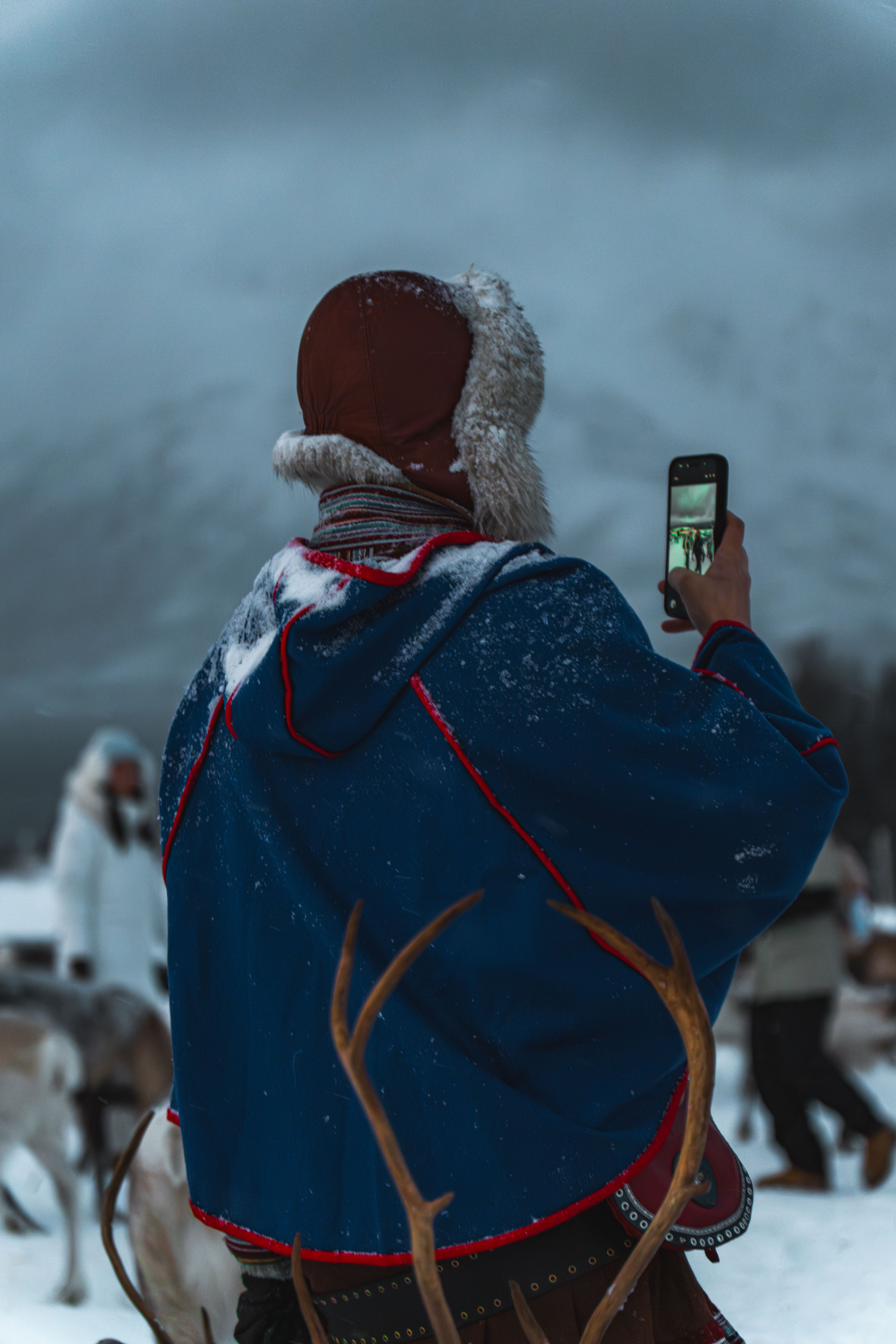 Sami herder in traditional blue gákti photographing reindeer