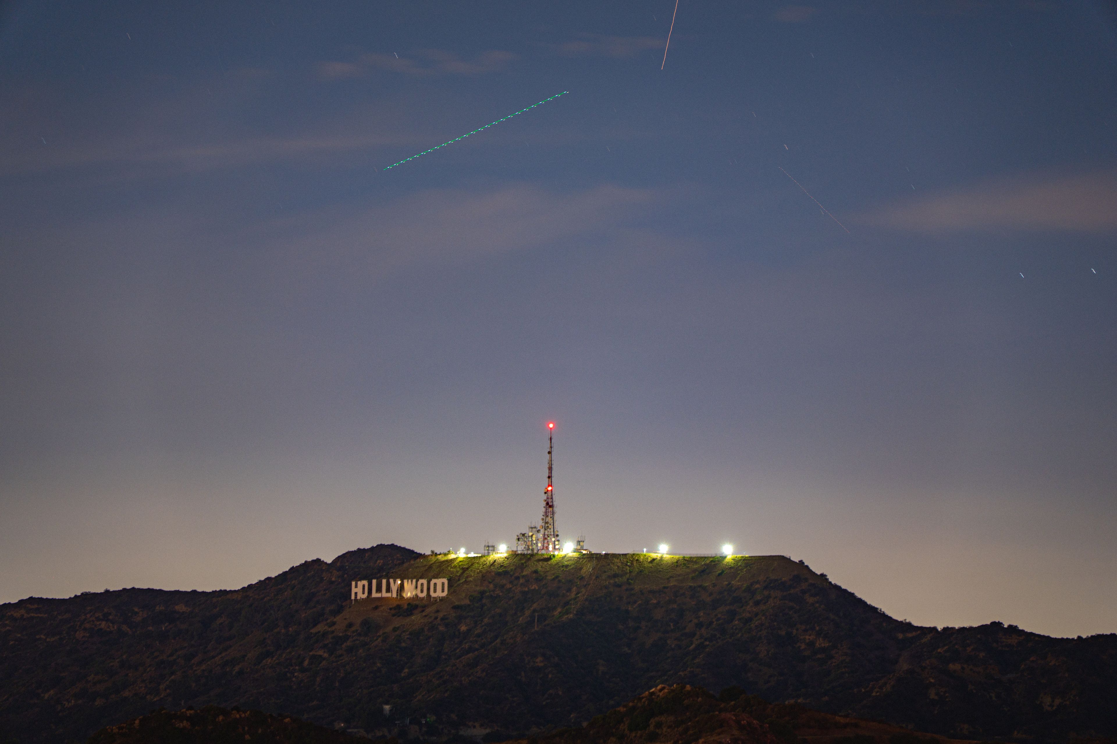 Hollywood sign at night with a plane trail streaking across the sky